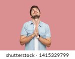 My God please help me. Portrait of hopeful sad handsome bearded young man in blue casual style shirt standing looking up and praying with worry face. indoor studio shot, isolated on pink background.