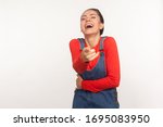 Small photo of You look ludicrous! Portrait of girl in denim overalls bursting into laughing and pointing finger to camera, teasing, making fun of ridiculous friend. indoor studio shot isolated on white background