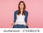 Poor student, unemployment. Portrait of upset jobless girl in checkered shirt turning out empty pockets, showing no money gesture, worried about debts. indoor studio shot isolated on pink background