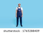 Full length worker man in blue overalls and cap standing, looking calm and positive at camera. Profession of service industry, house repair. indoor studio shot isolated on blue background