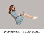 Small photo of Hovering in air. Pretty girl ruffle dress levitating, typing keyboard using laptop for work online, surfing web social networks while flying in mid-air. indoor studio shot isolated on gray background