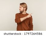 Small photo of Leave me! Portrait of upset vexed man with beard in sweatshirt pointing finger aside, ordering get out and looking resentful, boss dismissing from work, showing exit. indoor studio shot isolated