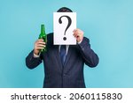 Portrait of anonymous person wearing dark official style suit hiding behind paper with question mark and holding bottle with alcohol. Indoor studio shot isolated on blue background.
