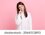 Small photo of Female touching nose, showing liar gesture, angry about falsehood, outright deception, fake news, wearing white casual style sweater. Indoor studio shot isolated on pink background.