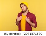 Small photo of Portrait of bearded guy in beanie hat and checkered shirt looking haughty at camera, pointing finger at himself, boasting victory, self-confident. Indoor studio shot isolated on yellow background.