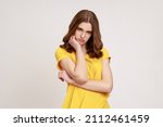 Small photo of Portrait of bored exhausted teenager girl with wavy hair in yellow t-shirt leaning on hand and looking at camera with disinterest, tired of boring film. Indoor studio shot isolated on gray background.