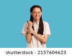 Small photo of Upset displeased woman with dreadlocks touches injured hand, shows problematic painful zone on wrist, suffers from terrible pain, wearing white shirt. Indoor studio shot isolated on blue background.