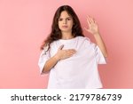 Small photo of I swear. Portrait of little girl wearing white T-shirt raising one hand and holding on chest another, swearing in honesty and devotion, patriotism. Indoor studio shot isolated on pink background.