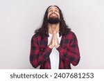 Small photo of Desperate man in checkered red shirt begging for mercy and crying, holding palms together, looking grievous while begging for something. Indoor studio shot isolated on gray background.
