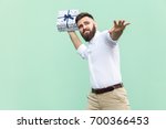 Small photo of Catch your gift! Young adult man swung and wants to throw off your gift box, isolated on light green background. Studio shot