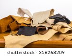 Small photo of Leftover pieces of rawhide; buckskin; doeskin; leather; cow hide and suede on old wooden work bench against white background with copy space.