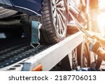 Small photo of Closeup of Vehicle Wheel Secured on the Tow Truck with Tie Down Straps for Safe Transportation. Breakdown Assistance. Automotive Industry.