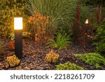 Outdoor Bollard Lamp Illuminating Colorful Plants in the Evening. Landscaped Garden Decorative Lighting Idea.