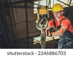 Professional Contractor Lowering the Load Using Large Lifting Hook of Overhead Crane. Indoor Construction Site in the Background. Industrial Theme.
