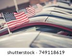 American Made Cars Sale Concept Photo. United States Economy and Market Theme. Brand New Vehicles For Sale with American Flags Attached. Dealership Lot.