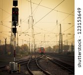 Small photo of Moble photography lo-fi styled image of a red commuter train on an urban railway track with confusing lines and overhead cables and a red signal light
