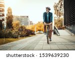 A handsome casual middle-aged businessman is going to the office by bicycle. He is driving bike in front of office district.