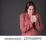 Small photo of A woman enjoying a cup of coffee in a tacky business suit on a grey background
