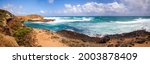 The Australian rocky coast is about 12 apostles. Strong winds drive ocean waves to the shore cliffs. A wide panorama. Sand dunes and cliffs. Blue sky with clouds on the horizon.