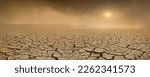 Wide panorama of barren cracked land with sun barely visible through the dust storm, drought and desertification concept