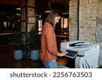 Small photo of Young woman employee working on printer at coworking office