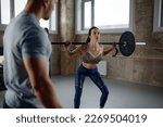 Young sportswoman lifting barbell under fitness instructor control