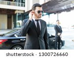 Handsome bodyguard listening to earpiece with car parked on street in city