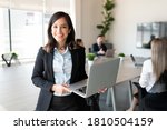 Portrait of smiling female entrepreneur holding a laptop with team in background at office conference room