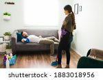 Small photo of Careless and slob man lying on a couch and watching TV while his wife does all the housework at home