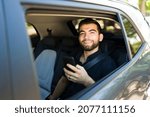 Small photo of Young man giving a good rating of a carpool service on his smartphone while sitting in the car back seat