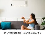 Frustrated young woman feeling worried about her broken air conditioner and remote control 