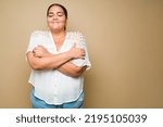 Small photo of Loving obese young woman giving herself a hug and with a lot of self esteem or love feeling happy against a yellow background
