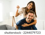 Handsome man piggybacking his girlfriend showing their new home keys after buying a house