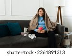 Sad overweight woman crying wrapped in a blanket while eating chocolate ice cream because of her sad breakup