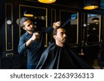 Small photo of Professional barber working at an elegant barber shop and cutting the hair of an attractive caucasian man