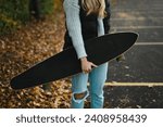 Close up of young woman holding longboard in parking lot with leaves