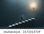 Way to success and creative idea concept with young woman climbing white stairs to big illuminated light bulb on dark grey wall