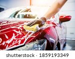 Worker washing red car with...