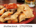 Closeup of a plate of pizza rolls with marinara sauce and beer in the background