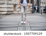 Small photo of Midsection of young blind man with white cane walking across the street in city.