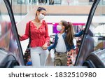 Small photo of Mother and daughter with face mask on escalator indoors in shopping center, coronavirus concept.