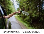 Woman's hand throwing away plastic bottle from car window on the road in green nature, environmental protection, global warming concept