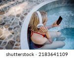 Rlaxed woman wearing headphones listening to music and sittin in hot tub, summer vacation concept.