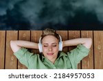 Rlaxed woman wearing headphones listening to music lying on a pier by natureal lake in summer