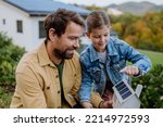 Small photo of Little girl with her dad holding paper model of house with solar panels, explaining how it works.Alternative energy, saving resources and sustainable lifestyle concept.
