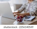 Side view of woman holding bowl with grapes above desk with computer, diary and smartphone. Work-life balance concept.