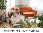 Senior woman resting with cup of tea in her living room, listening music.