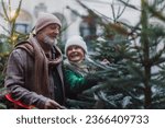 Happy senior couple enjoying christmas market, buying christmas tree.