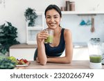 Shot of athletic smiling woman drinking smothie while listening music with earphones in the kitchen at home.
