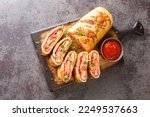 Italian stromboli, delicious pizza roll filled with sausage and ham closeup on the wooden board on the table. Horizontal top view from above
